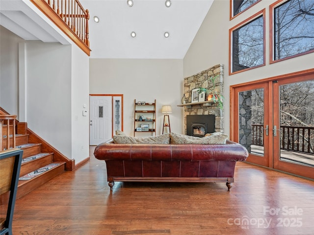 living area featuring high vaulted ceiling, a fireplace, wood finished floors, french doors, and stairway