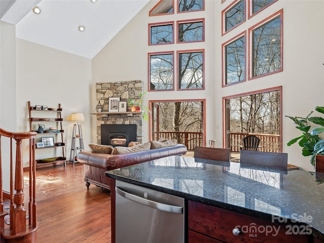 kitchen with high vaulted ceiling, a fireplace, wood finished floors, dishwasher, and dark stone countertops