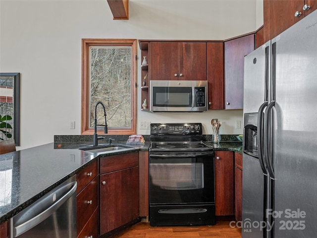 kitchen with wood finished floors, a sink, a healthy amount of sunlight, appliances with stainless steel finishes, and dark stone counters