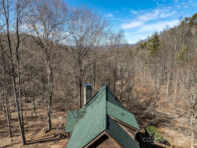 exterior space with a forest view, a chimney, and roof with shingles