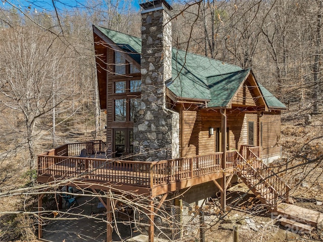 view of side of property featuring a shingled roof, a chimney, and a wooden deck