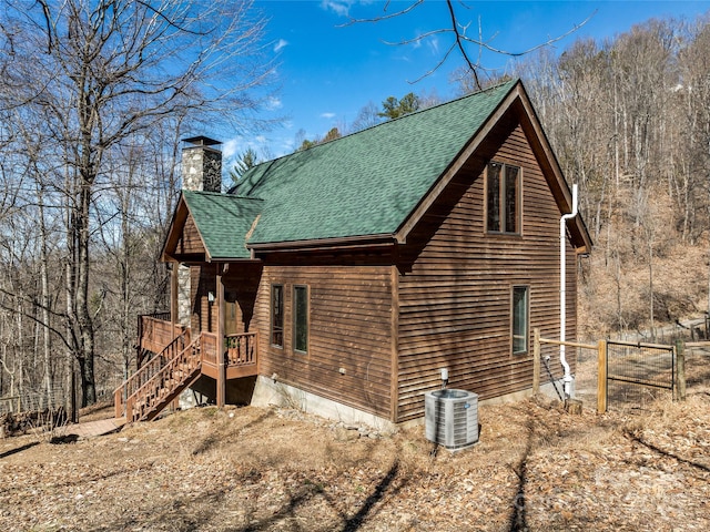 view of side of home featuring a shingled roof, a chimney, and central air condition unit