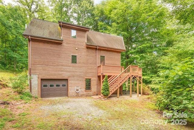 view of front of property featuring driveway, stairway, roof with shingles, an attached garage, and a wooden deck