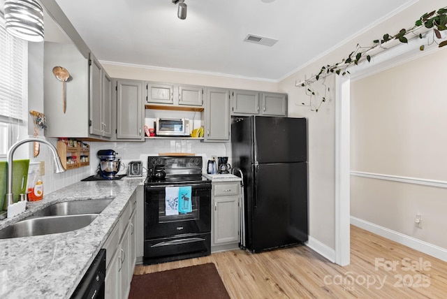 kitchen with decorative backsplash, light stone counters, light wood-type flooring, black appliances, and a sink