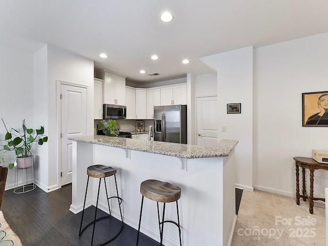 kitchen with a kitchen bar, white cabinetry, tasteful backsplash, light stone counters, and appliances with stainless steel finishes