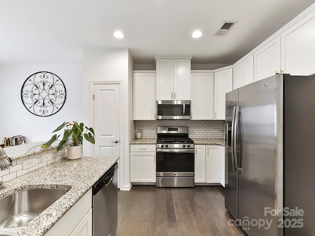 kitchen with appliances with stainless steel finishes, white cabinetry, sink, dark hardwood / wood-style flooring, and light stone countertops