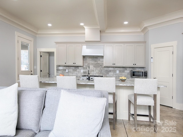 kitchen featuring wall chimney exhaust hood, light stone countertops, a kitchen island with sink, and decorative backsplash