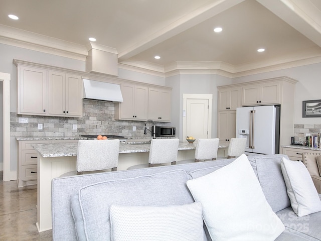 kitchen with appliances with stainless steel finishes, a breakfast bar, an island with sink, light stone counters, and custom range hood