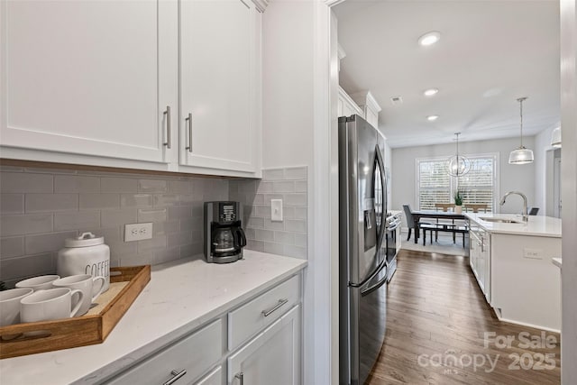 kitchen featuring pendant lighting, sink, stainless steel fridge, white cabinets, and light stone counters