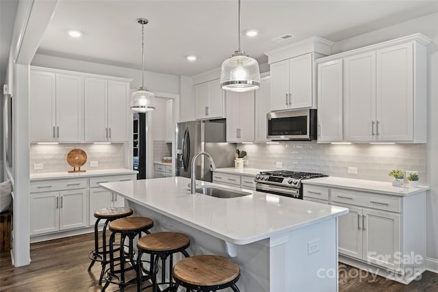 kitchen with pendant lighting, sink, stainless steel appliances, white cabinets, and a center island with sink