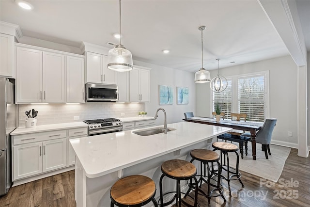 kitchen with stainless steel appliances, hanging light fixtures, sink, and a kitchen island with sink