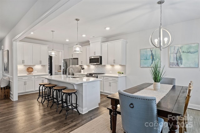 kitchen with dark hardwood / wood-style floors, white cabinets, hanging light fixtures, stainless steel appliances, and a center island with sink