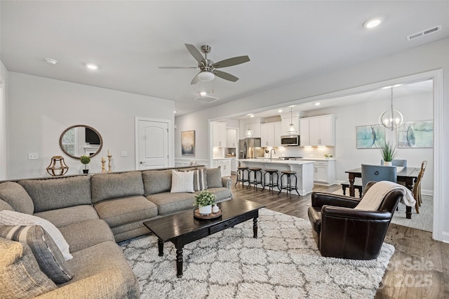 living room featuring dark wood-type flooring and ceiling fan with notable chandelier