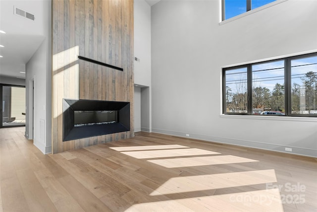 unfurnished living room featuring a high ceiling, a large fireplace, a wealth of natural light, and light wood-type flooring