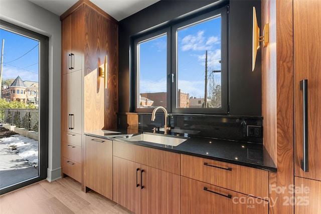 kitchen with sink, dark stone countertops, and light wood-type flooring