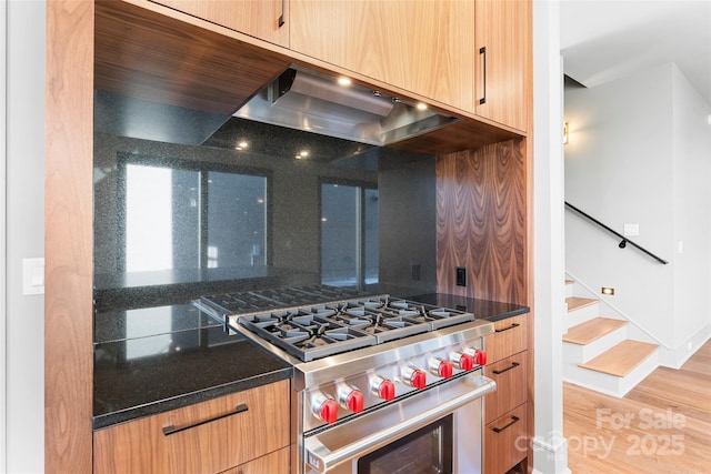 kitchen featuring range hood, dark stone countertops, decorative backsplash, stainless steel range, and light wood-type flooring