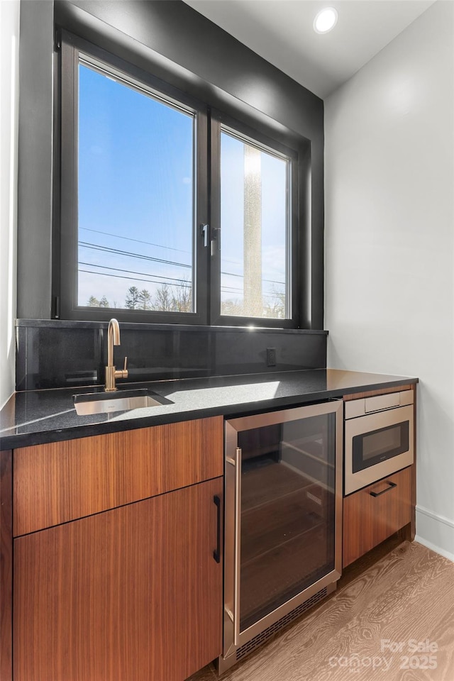 kitchen featuring stainless steel microwave, beverage cooler, light hardwood / wood-style floors, and wet bar