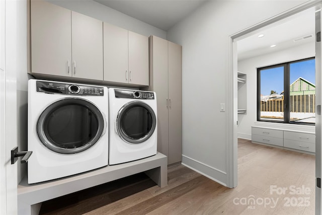 laundry area with cabinets, washing machine and clothes dryer, and light hardwood / wood-style floors