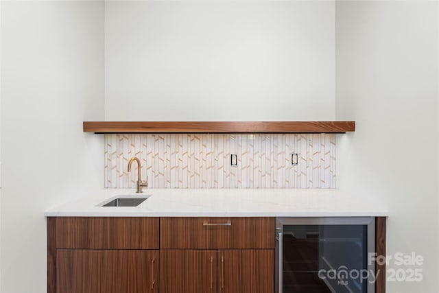 bar with tasteful backsplash, light stone countertops, sink, and beverage cooler