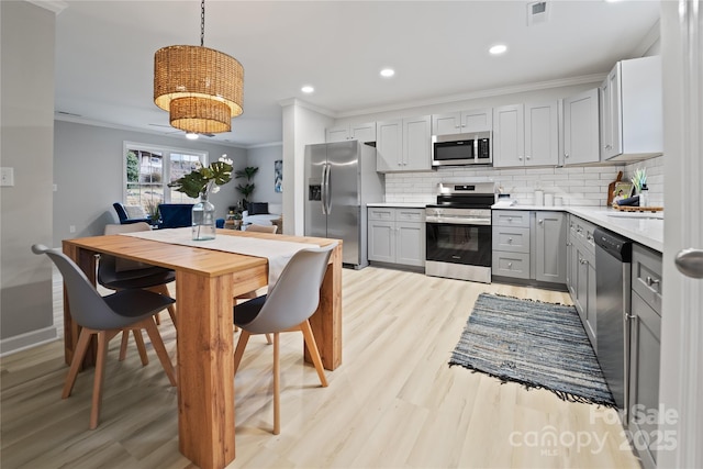 kitchen featuring pendant lighting, tasteful backsplash, gray cabinetry, stainless steel appliances, and crown molding