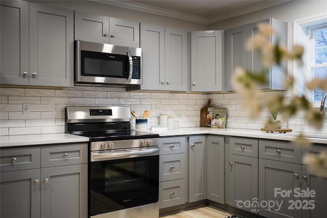 kitchen with crown molding, light wood-type flooring, appliances with stainless steel finishes, gray cabinets, and backsplash