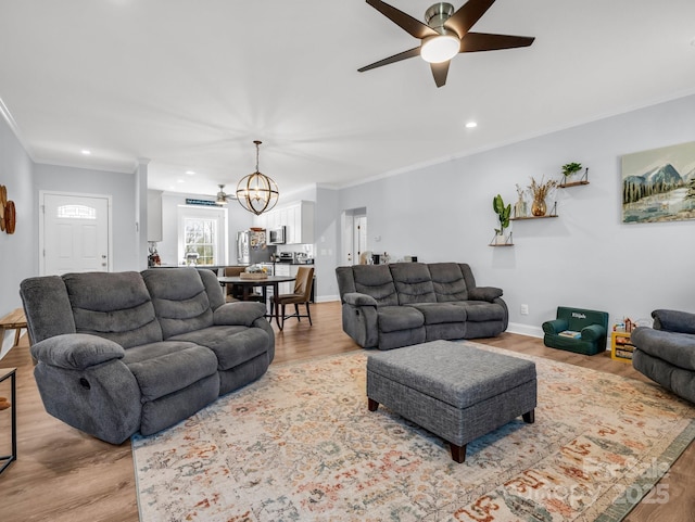 living room featuring ceiling fan with notable chandelier, light hardwood / wood-style flooring, and crown molding