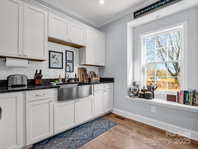 kitchen featuring white cabinetry, sink, tasteful backsplash, dark stone countertops, and crown molding