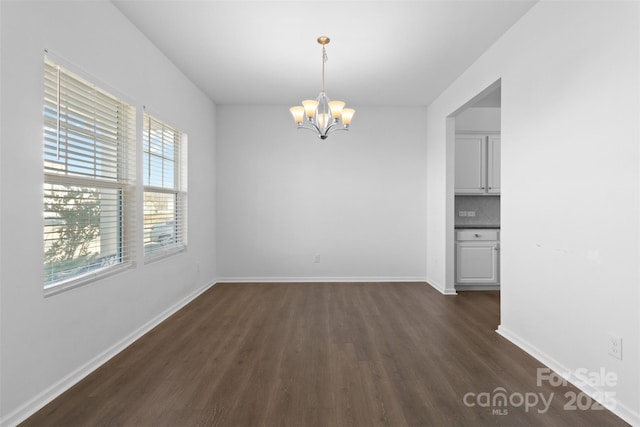 unfurnished dining area featuring a chandelier, dark wood-style flooring, and baseboards