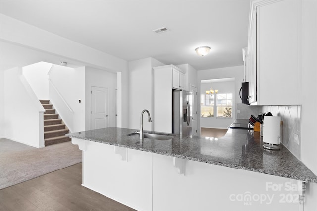 kitchen with a peninsula, a sink, visible vents, white cabinetry, and stainless steel refrigerator with ice dispenser