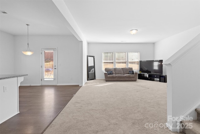 unfurnished living room featuring dark wood-style floors, dark colored carpet, baseboards, and a healthy amount of sunlight