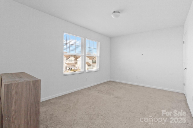 spare room featuring light colored carpet and baseboards