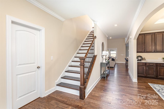 staircase with ornamental molding, arched walkways, baseboards, and wood finished floors