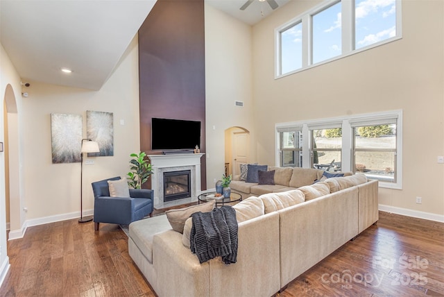 living room with baseboards, a fireplace, arched walkways, and wood finished floors