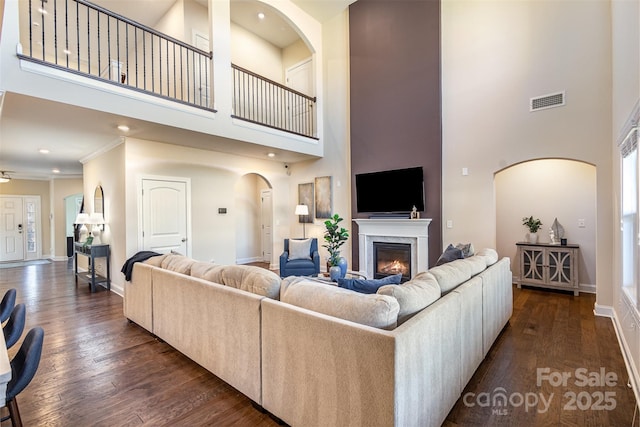 living room featuring baseboards, visible vents, dark wood finished floors, and a glass covered fireplace