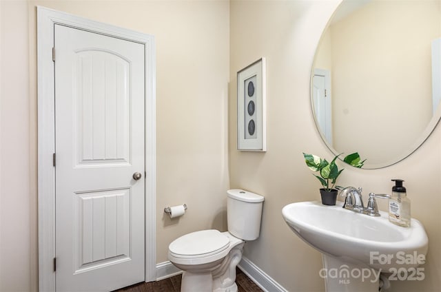 half bath featuring a sink, toilet, and baseboards