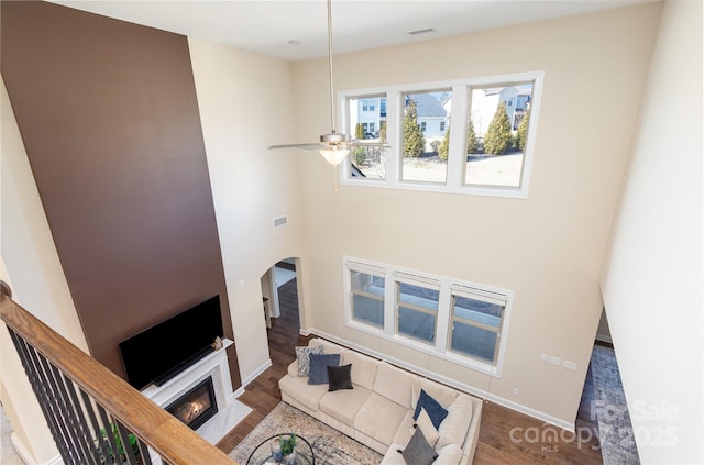 living area featuring a fireplace with flush hearth, arched walkways, wood finished floors, and a ceiling fan