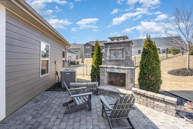 view of patio / terrace featuring fence, an outdoor stone fireplace, central AC, and a residential view