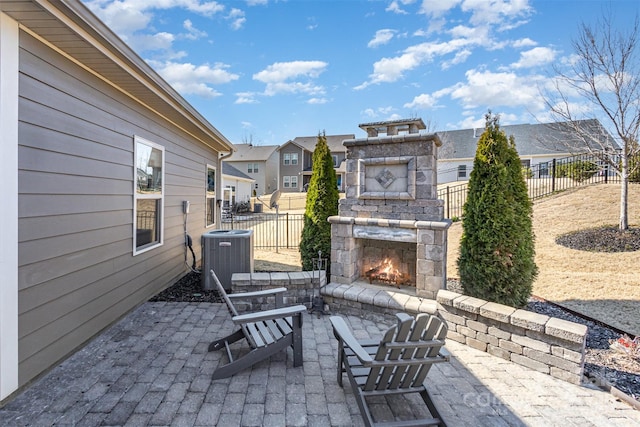 view of patio with central AC unit, fence, an outdoor stone fireplace, and a residential view