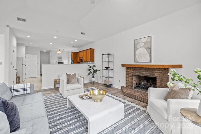 living room with lofted ceiling, light hardwood / wood-style floors, and a brick fireplace