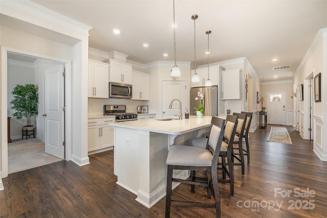 kitchen with visible vents, appliances with stainless steel finishes, a kitchen breakfast bar, a kitchen island with sink, and a sink