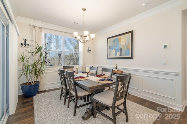 dining space featuring wainscoting, ornamental molding, dark wood-type flooring, a chandelier, and a decorative wall