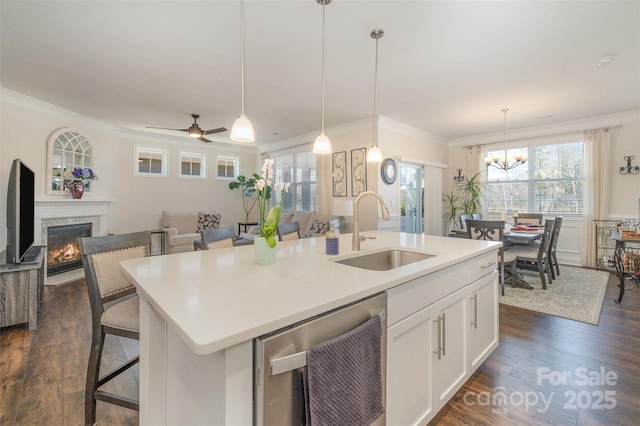 kitchen featuring a warm lit fireplace, white cabinets, an island with sink, ornamental molding, and a sink