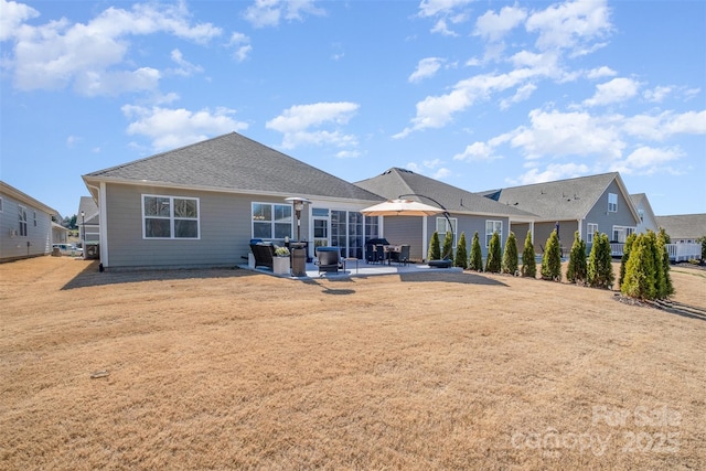 back of house with a yard, roof with shingles, and a patio