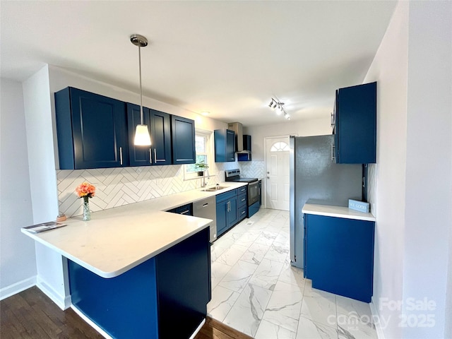 kitchen with pendant lighting, stainless steel appliances, blue cabinets, kitchen peninsula, and wall chimney exhaust hood