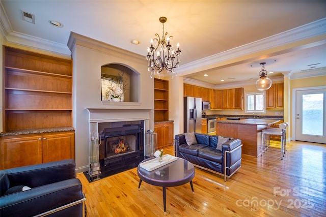 living room with a tiled fireplace, ornamental molding, light wood-type flooring, and built in shelves