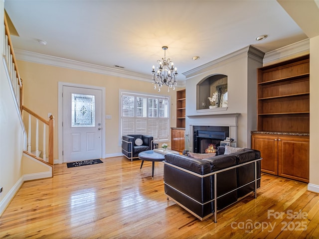 living room featuring crown molding, a chandelier, built in shelves, and light hardwood / wood-style floors