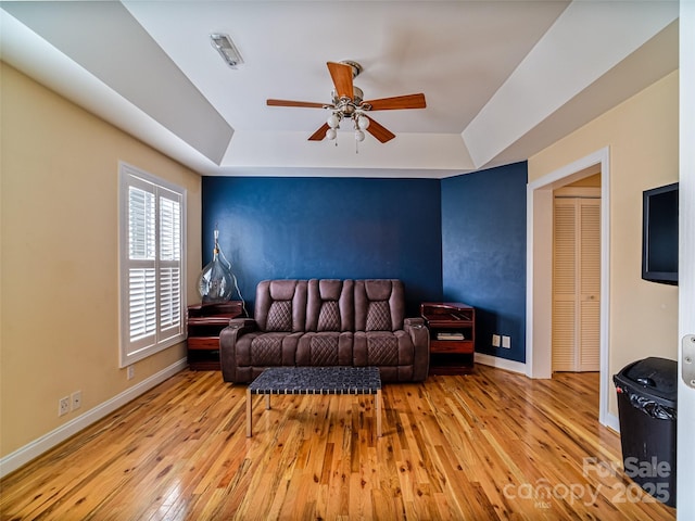 living room featuring light hardwood / wood-style floors, a raised ceiling, and ceiling fan