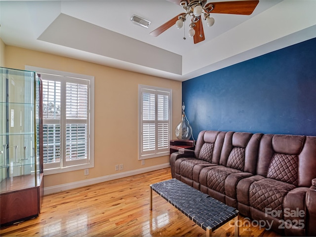 living room with a tray ceiling, light hardwood / wood-style flooring, and ceiling fan