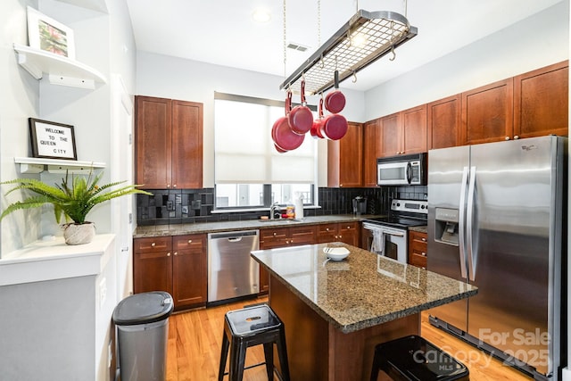 kitchen with appliances with stainless steel finishes, sink, a kitchen island, dark stone counters, and decorative backsplash