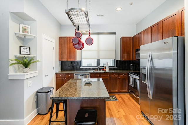 kitchen featuring a kitchen island, tasteful backsplash, dark stone counters, appliances with stainless steel finishes, and a kitchen breakfast bar